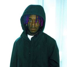 a young man with dreadlocks standing in front of a white wall wearing a black jacket