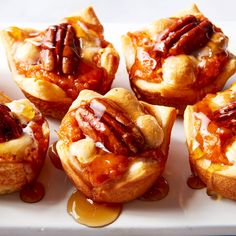 several mini pecan pies with caramel sauce and pecans on top, sitting on a white platter