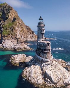 an aerial view of a lighthouse in the middle of the ocean with mountains in the background