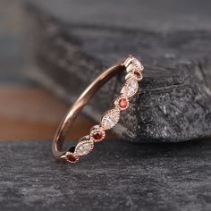 a rose gold ring with two red stones on top of it, sitting on a rock