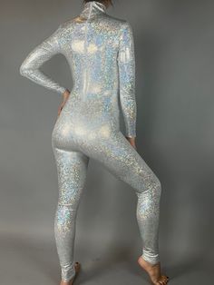 Command the spotlight in our Holographic Silver Catsuit! Designed for dancers, aerialists, and performers, this eye-catching full-body catsuit features a stunning holographic, broken glass design. With a turtleneck, long sleeves, and a convenient back zipper, this silver catsuit offers both style and functionality. Mesmerizing Shine: The holographic effect creates a dazzling, reflective appearance that catches the light as you move. Secure Fit: The snug fit and stretchy fabric ensures comfort an Metallic Shiny High Stretch Unitard, Futuristic Fitted Bodysuit For Night Out, Stretch Shiny Bodysuit For Party, High Neck Unitard With Thumbholes, Silver Shiny Stretch Bodysuit, Metallic Stretch Unitard For Night Out, High Neck High Stretch Unitard For Night Out, Metallic High Stretch Unitard For Party, High Neck Unitard With High Stretch For Night Out