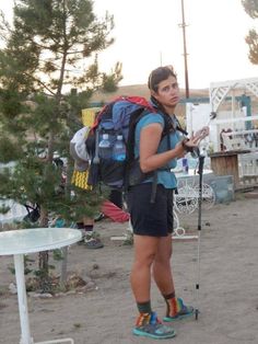 a man with a backpack and hiking poles standing in the dirt near a table outside