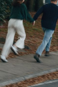 two people are walking down the sidewalk holding hands and one person is wearing white pants