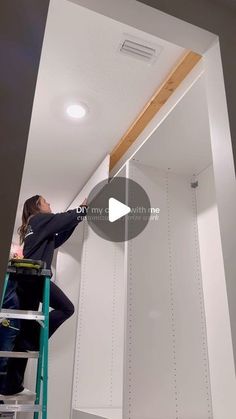 a man on a ladder painting the ceiling in a room with white walls and ceilings