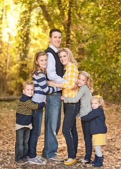 a family posing for a photo in the woods with leaves on the ground and trees behind them