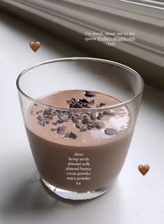 a glass filled with chocolate pudding on top of a white table next to some hearts