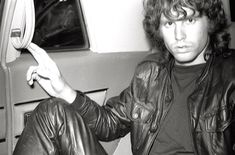 black and white photograph of man in leather jacket sitting on seat holding up banana peel