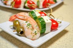 shrimp and vegetable skewers with olives on a white plate, ready to be served