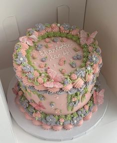 a birthday cake with pink frosting and flowers on the top is in a box