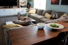 a wooden table topped with two white bowls filled with food and a glass of wine