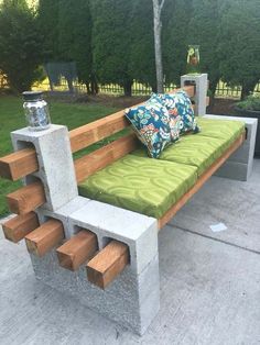 a bench made out of concrete blocks with green cushions and pillows on the seat area