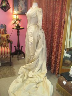 "1880's, 34\" bust, ecru silk faille, bustled and trained skirted wedding gown. A 19th century take on an 18th century lace up, low cut bodice. Bodice has a sharply pointed bottom, below waist, and 3/4 length cuffed sleeves. The bodice curves over hips, and is shorter in back than front. Bustled skirt has steel covered hoops built into back of skirt , and elaborate drapery forming into a long long train. Skirt has scalloped edge at bottom of the front, the bottom of train has a covered dust ruff Victorian Ball Gown Dress For Wedding, Fitted Victorian Ball Gown For Wedding, Fitted Victorian Dress For Debutante Ball, Historical Ball Gown Wedding Dress, Wedding Victorian Dress With Boned Bodice, Victorian Style Crinoline Ball Gown Dress, Vintage Victorian Ball Gown With Boned Bodice, Fitted Cream Victorian Ball Gown, Victorian Ball Gown For Debutante Ball