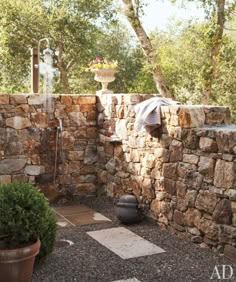 an outdoor shower in the middle of a stone walled area with potted plants on either side