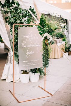 a sign that is sitting in the middle of a sidewalk with plants and flowers around it