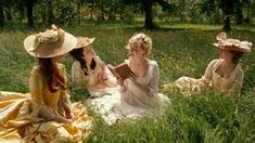 three women sitting in the grass with hats on their heads and one reading a book