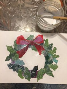 a paper wreath with red and green leaves on it next to a glass jar filled with water