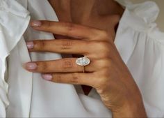 a woman's hand with a diamond ring on her left hand, wearing a white shirt