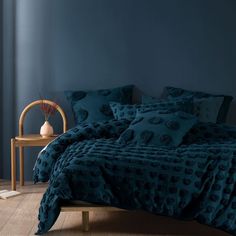 a bed with blue comforters and pillows in a room next to a wooden chair