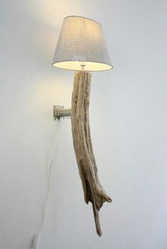 a lamp that is on the wall next to a tree branch with a white shade