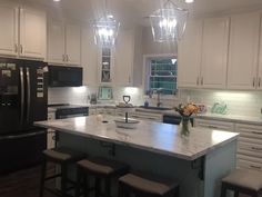 a large kitchen with white cabinets and marble counter tops is lit by pendant lights above the island