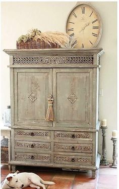 an old dresser with a clock on top and a dog laying in the floor next to it