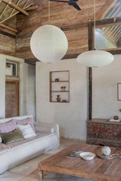 a living room filled with furniture and two white lamps hanging from the ceiling over a wooden table