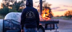 a man in a hoodie standing next to a trailer with an open fire on it