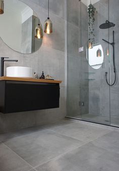 a bathroom with a sink, mirror and shower stall in grey tile flooring next to a white toilet