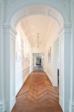 an archway leading to another room with wood floors and white walls, along with a chandelier hanging from the ceiling