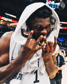 a man in a white hoodie holding his hands up to his face while standing on a basketball court