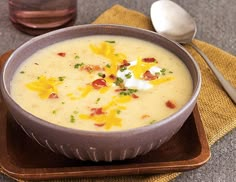 a bowl of soup with cheese and bacon in it on a plate next to a spoon