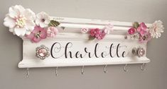 a white sign with pink flowers hanging from it's sides and hooks on the wall