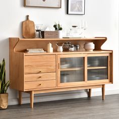 a wooden cabinet with glass doors and shelves on the top, next to a potted plant