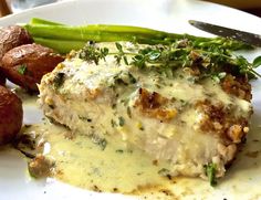 a white plate topped with meat covered in gravy next to potatoes and asparagus