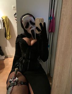 a woman in a costume is taking a selfie with her cell phone while wearing a mask