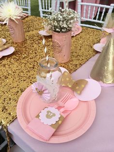 a table set up with pink and gold plates, napkins, cups and vases