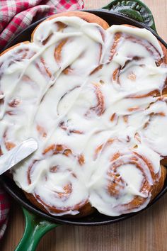 a green cast iron skillet filled with cinnamon rolls covered in white icing on top of a wooden table