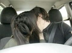 two people sitting in the back seat of a car, one is kissing the other