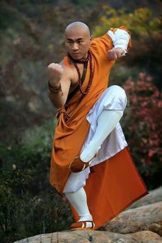 a man in an orange and white outfit standing on rocks with his arms out to the side