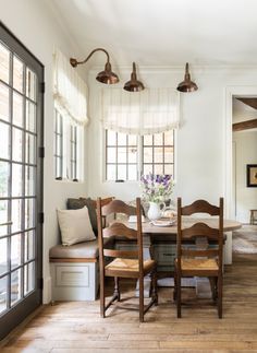 a dining room table with four chairs and a bench in front of the window that is open