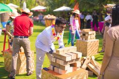 a man in white shirt and tie standing next to wooden blocks on grass with people behind him