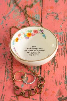 a small bowl with a chain around it on a pink table next to a necklace