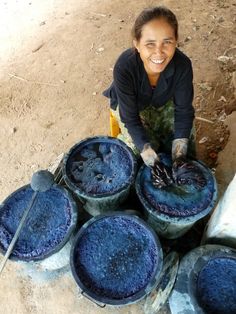 a woman is sitting on the ground next to buckets filled with blue stuff and smiling