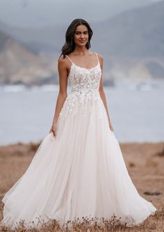 a woman standing on top of a sandy beach wearing a white dress with floral appliques