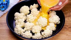 a person pouring orange juice over cauliflower in a black bowl on a wooden table