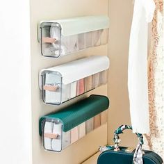 three plastic storage containers are hanging on the wall next to a purse and toiletries