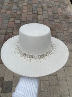 -Made in Guanajuato, Mexico -One size fits most -Stretch band to fit sizes S-L -Manmade -Shipped from Florida -15 in. L -14 in. W -6 in. H -Material felt -4 in. H Crown -hand decorated hat with shiny hat band with beautiful pearls  -This hat is perfect to add that extra touch to any outfit, and the perfect gift for brides ! Tea Party Outfit With Hat, White Hats For Women, Decorated Fedora Hats, Luxury White Boater Hat, Luxury White Brimmed Boater Hat, Luxury White Fedora For Western-themed Events, Pearl Hat Band, White Fedora Sun Hat For Western-themed Events, Hat Decorating Ideas