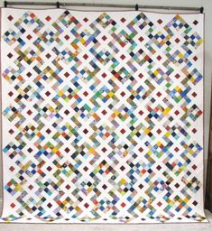 a white quilt with multicolored squares on the top and bottom, hanging from a wall