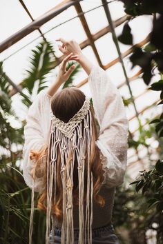 a woman with long red hair wearing a white blouse and fringed headband in a greenhouse