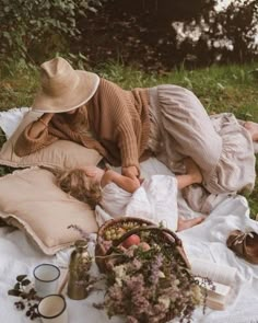 two women laying on a blanket in the grass next to some flowers and other items